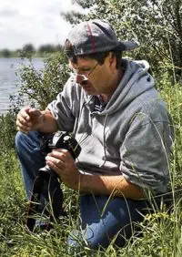 Der Fotograf Volker Röös im hohen Gras kniend, während er einige Einstellungen an seiner Kamera vornimmt